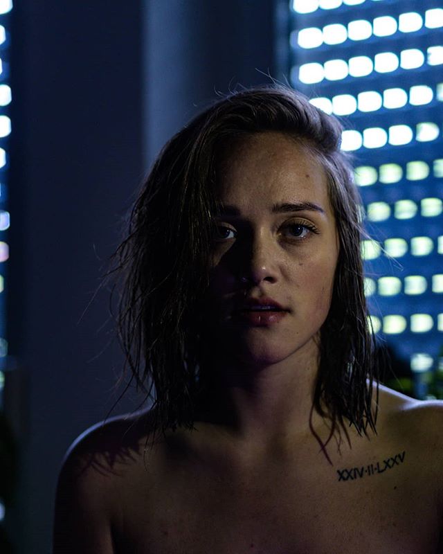 Striking portrait of a woman with a tattoo, captured in a moody, intimate studio setting with soft, artificial lighting.