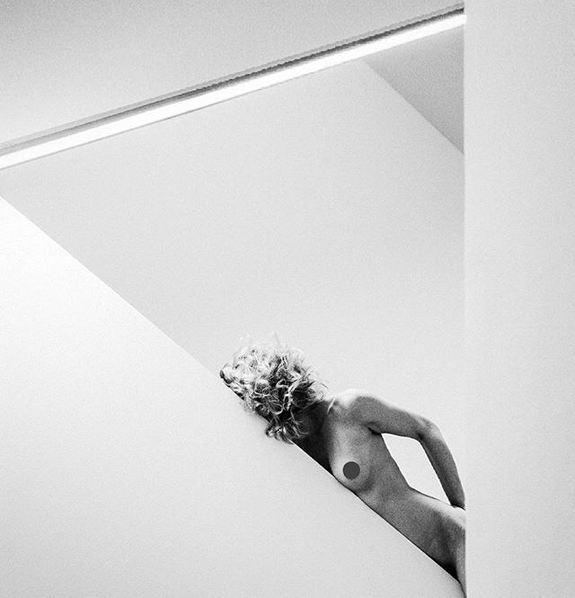 Artistic black and white nude portrait of a woman in a minimalist studio setting. 
