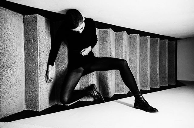 A woman in all black attire poses on stairs in a dramatic, black and white, editorial-style image.
