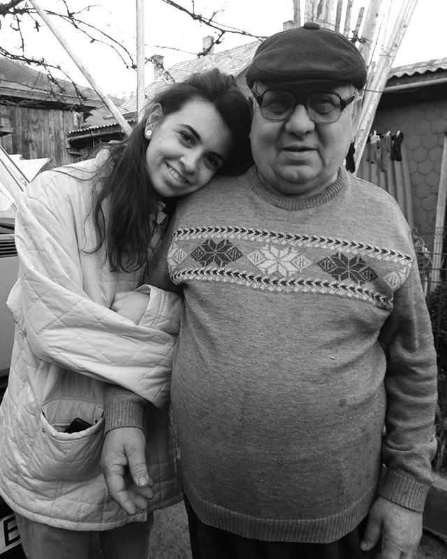 A young woman affectionately leans on an older man in a warm, monochrome outdoor portrait.
