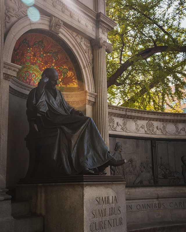 A statue of Samuel Hahnemann, also known as the Thinker, in a plaza with trees and artwork.