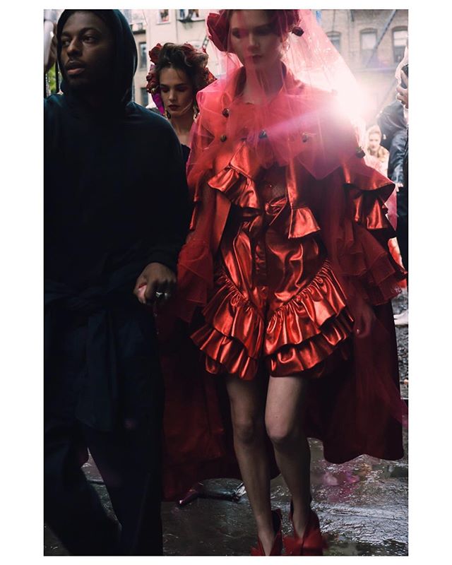 A model in a red ruffled outfit is walking down a city street during a fashion event.