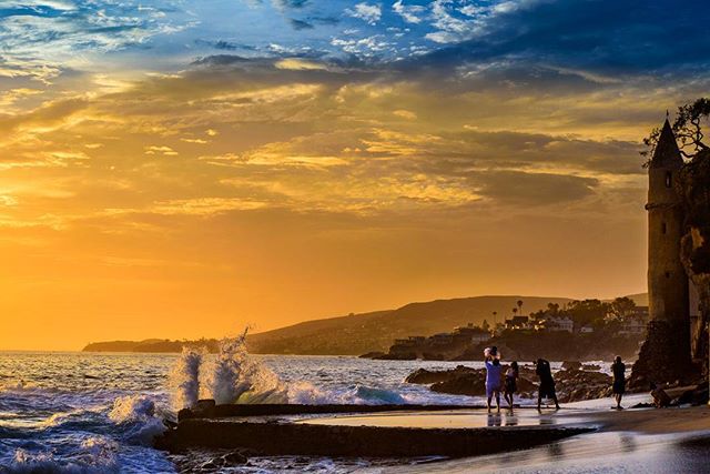 A picturesque sunset view of the beach, with a tower, waves, and people enjoying the tranquil scenery.