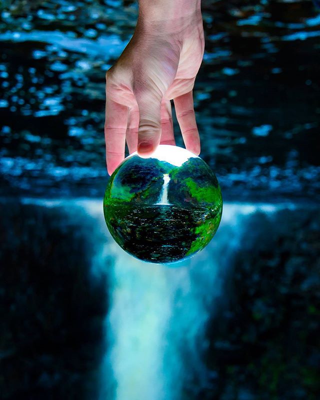 A surreal shot of a hand holding a globe containing a waterfall landscape, promoting nature's beauty and conservation.