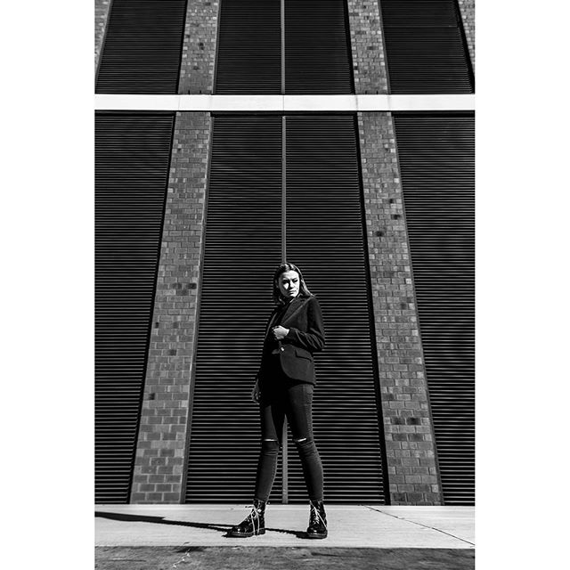 A stylish woman poses in front of an urban building, captured in a monochrome editorial fashion style.