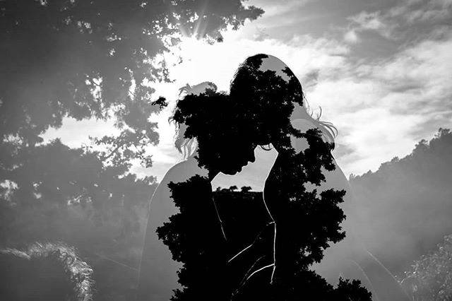 Two people embrace as a couple in a dreamy silhouette, artful double exposure against a natural sky.