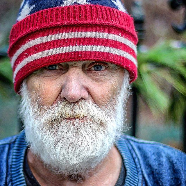 Portrait of a serious older man with a white beard wearing a patriotic hat.