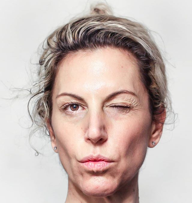 A woman winks playfully at the camera in a close-up portrait against a neutral background.