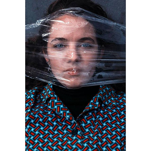 Intense portrait of a woman's face obscured by plastic wrap, highlighting emotion and mystery.