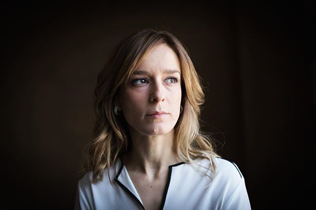 A woman looks thoughtfully to the side in a softly lit portrait, conveying a sense of seriousness and contemplation.