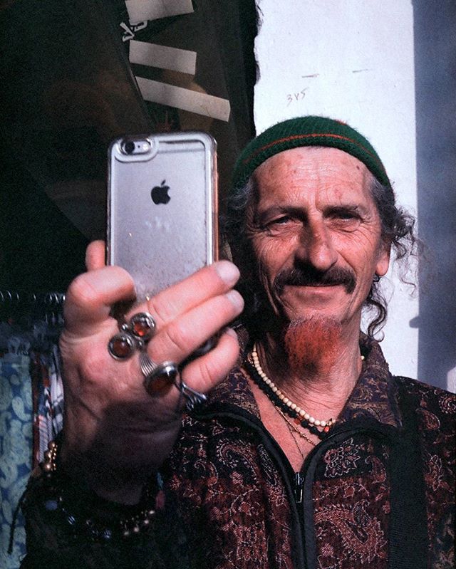 A smiling man with a beard and green beanie takes a selfie with his iPhone.