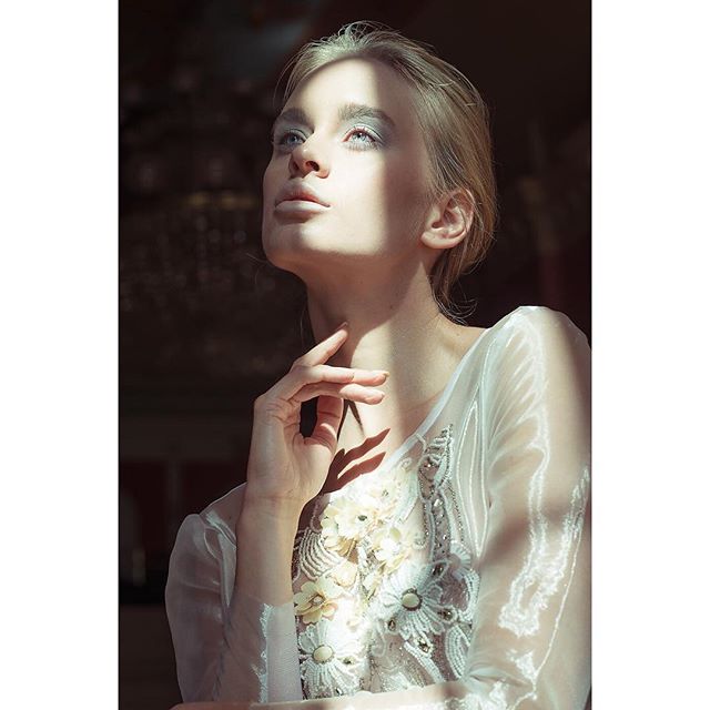 An elegant blond woman poses in soft light, showcasing a delicate, dreamy fashion style for advertising.