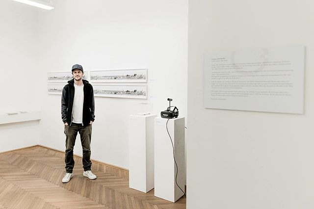 A man stands in a modern art gallery with vr headset exhibit and landscape art.