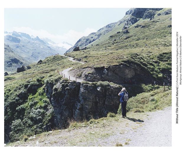 A person stands on a mountain path in a serene landscape, enjoying the natural scenery.