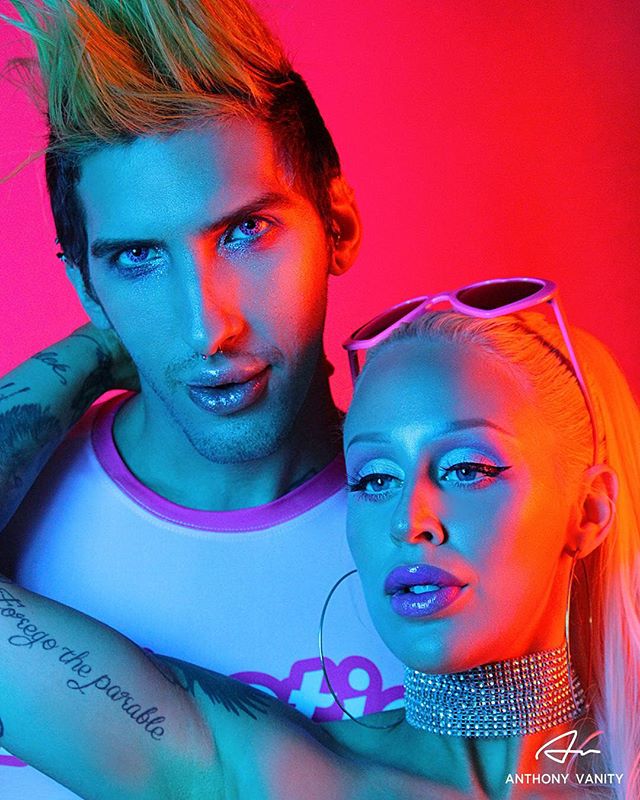 A stylish man and woman pose in a vibrant, brightly lit studio environment with a modern editorial aesthetic.
