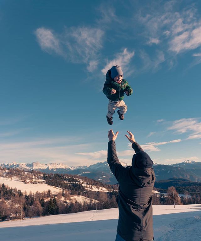 A father throws his child into the air on a snowy mountain, creating a joyful and playful moment.