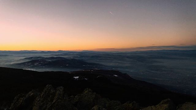 A serene landscape image featuring mountains fading into the horizon under a pastel sunrise sky with fog.