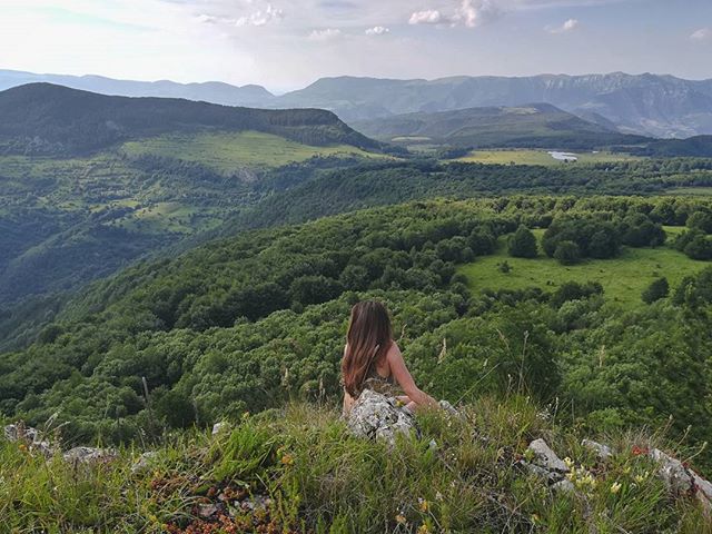 A woman enjoys the peaceful scenery from a mountain top overlooking the green landscape.