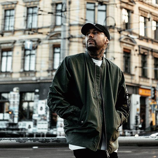 A stylish man in a bomber jacket stands on a city street, looking confident against an urban backdrop.