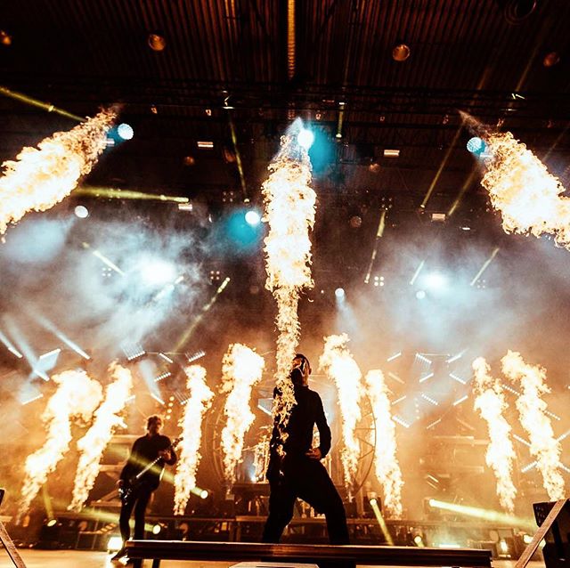 A musician on stage performs with fire effects, creating an intense and energetic atmosphere during a live concert.