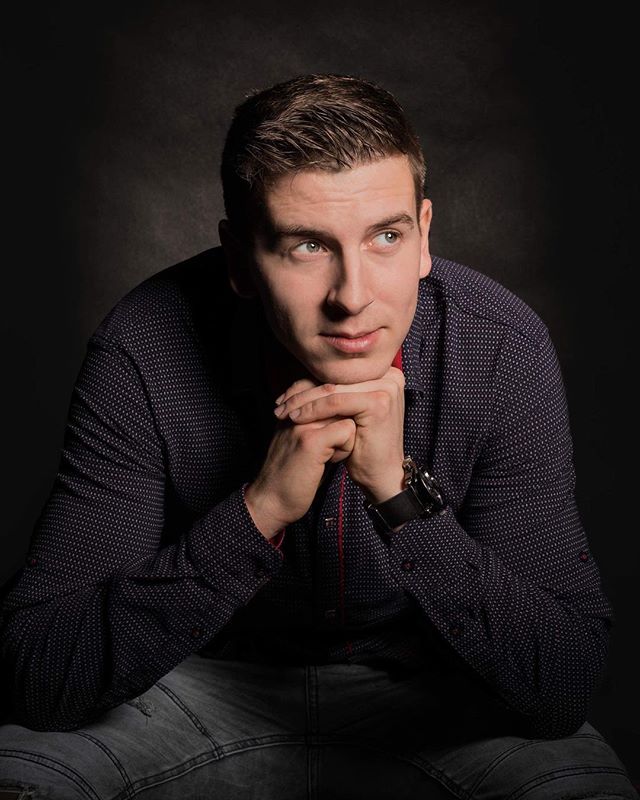 A man in a collared shirt poses thoughtfully against a dark backdrop.