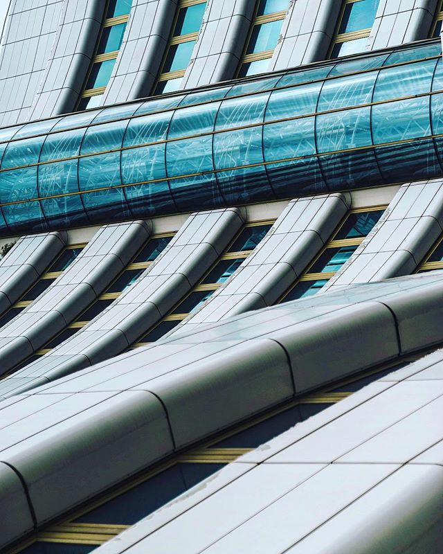 Abstract architectural detail featuring a modern building facade with glass skywalk and geometric window patterns.