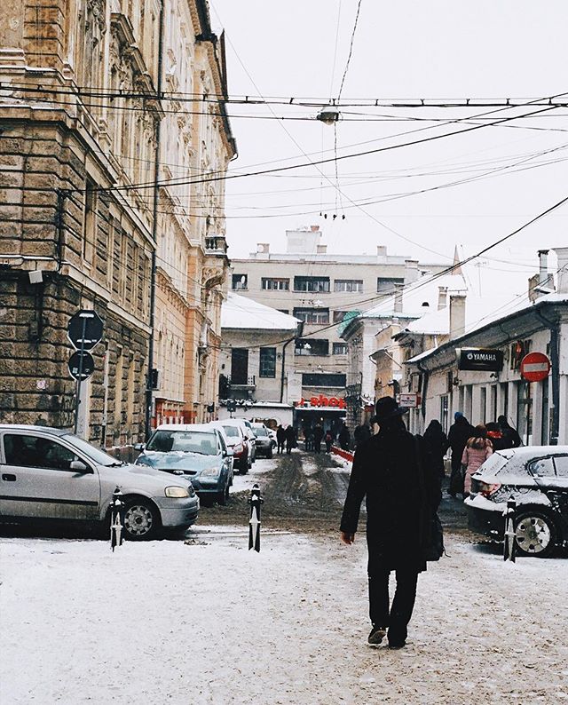 A man walks down a snowy street lined with buildings and cars on a winter day.