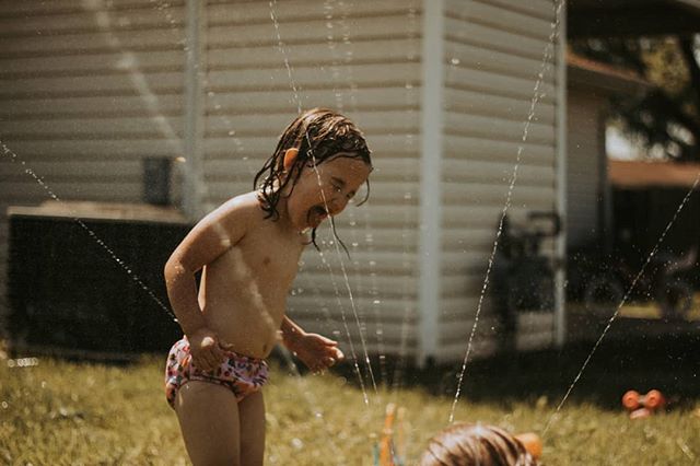 A young girl plays in a sprinkler on a sunny day in her backyard, enjoying a moment of summer fun.