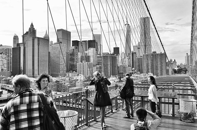 A black and white view of New York city from the Brooklyn Bridge with people enjoying the views.