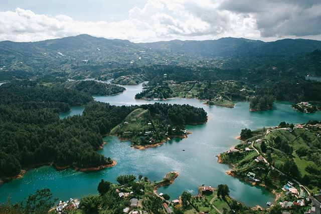 Aerial view of Guatape, Colombia featuring a beautiful lake with islands, houses, and rolling hills under a cloudy sky.
