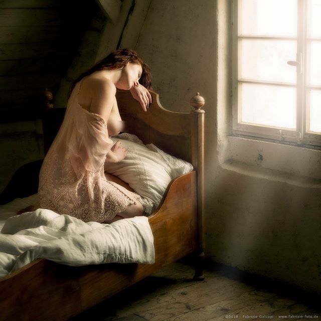 A woman rests on a bed in a dreamy, vintage-style bedroom with soft lighting.