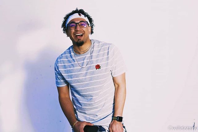 A cheerful man with glasses and a striped shirt smiles in a studio setting.