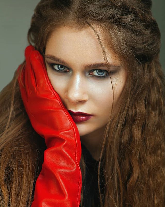 A beautiful woman with a red glove poses for a moody, intense portrait in a studio setting.
