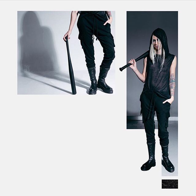 A woman poses with a baseball bat in a streetwear fashion editorial, wearing a hoodie, sweatpants, and combat boots.