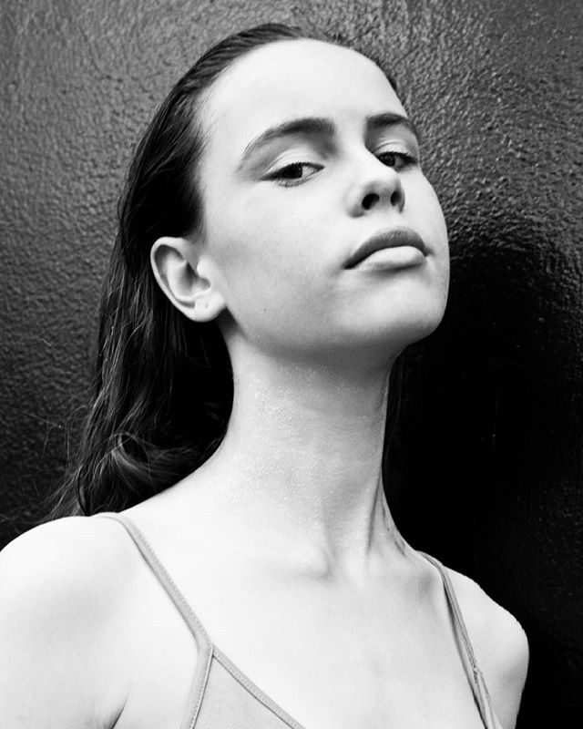 Monochrome portrait of a young woman with slicked-back hair, looking confidently upward against a dark textured background.