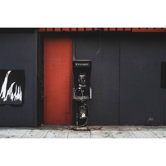 An old payphone stands on a city street with graffiti, showcasing urban decay and a bygone era.