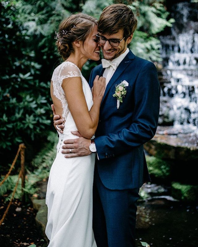 A happy couple embraces in front of a waterfall on their wedding day, exuding love and joy.