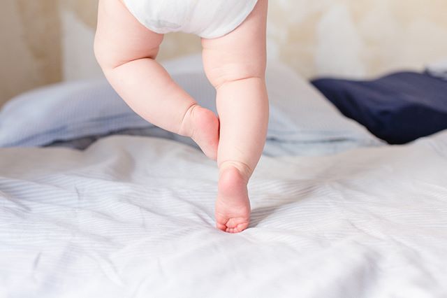 A baby wearing a diaper takes its first steps on a soft bed.