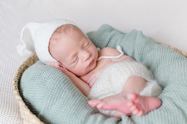 A newborn baby sleeps peacefully in a basket with a knitted hat and blanket, capturing a tender moment.