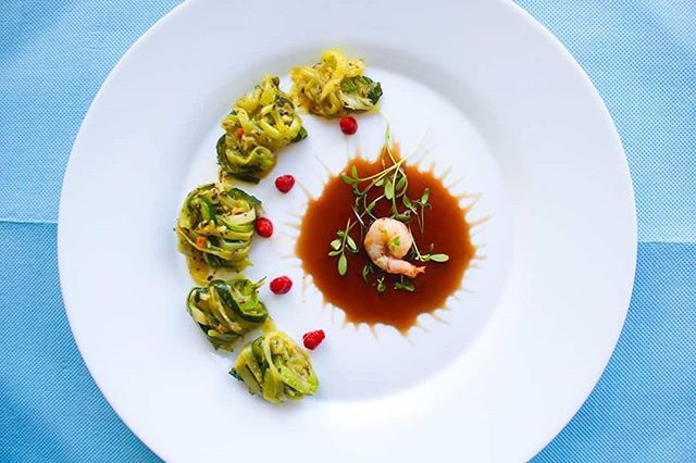 Elegant plate featuring shrimp, zucchini, and microgreens in a brown sauce.