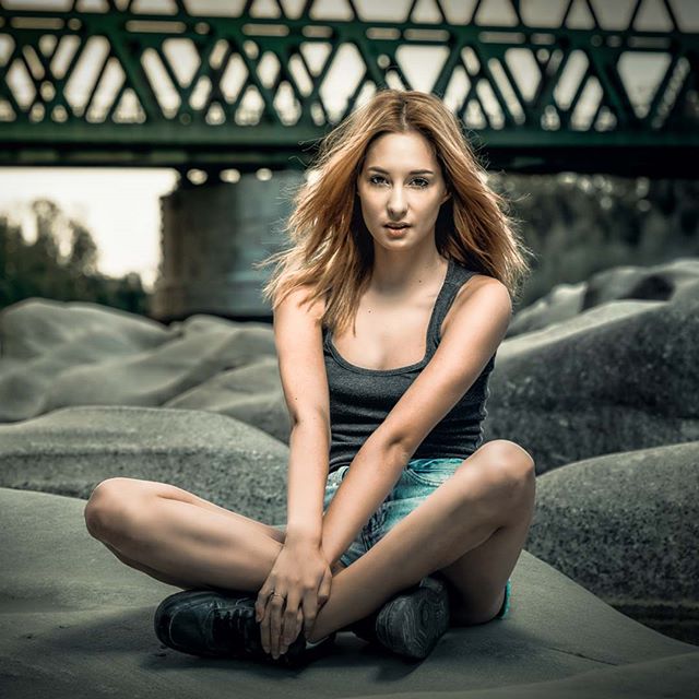 A woman sits cross-legged on rocks with a bridge in the background.