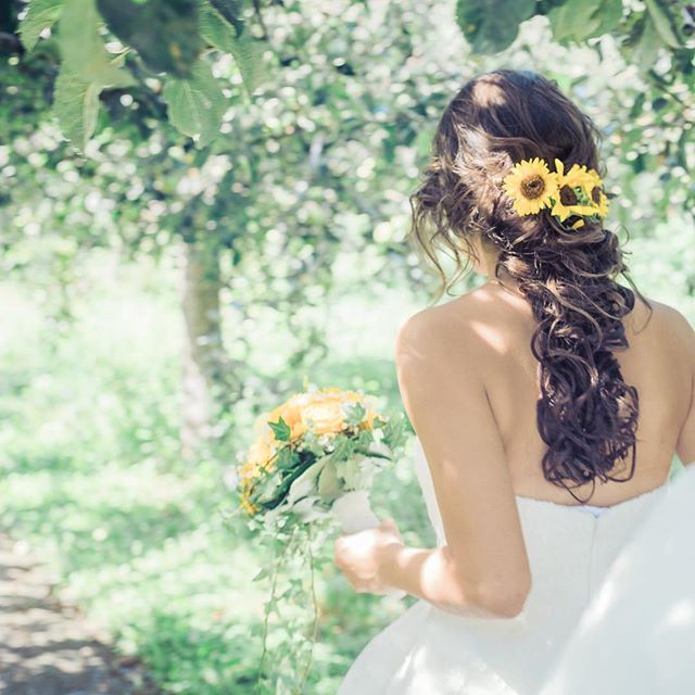 A bride in a white dress, holding a bouquet of flowers, with sunflowers in her hair, walks in a garden.