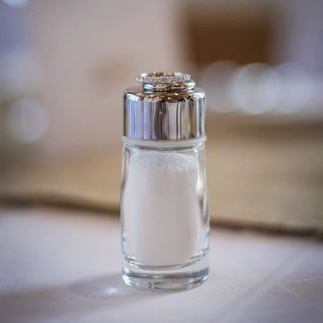A wedding ring rests on a salt shaker, symbolizing an engagement announcement in a minimalist style.
