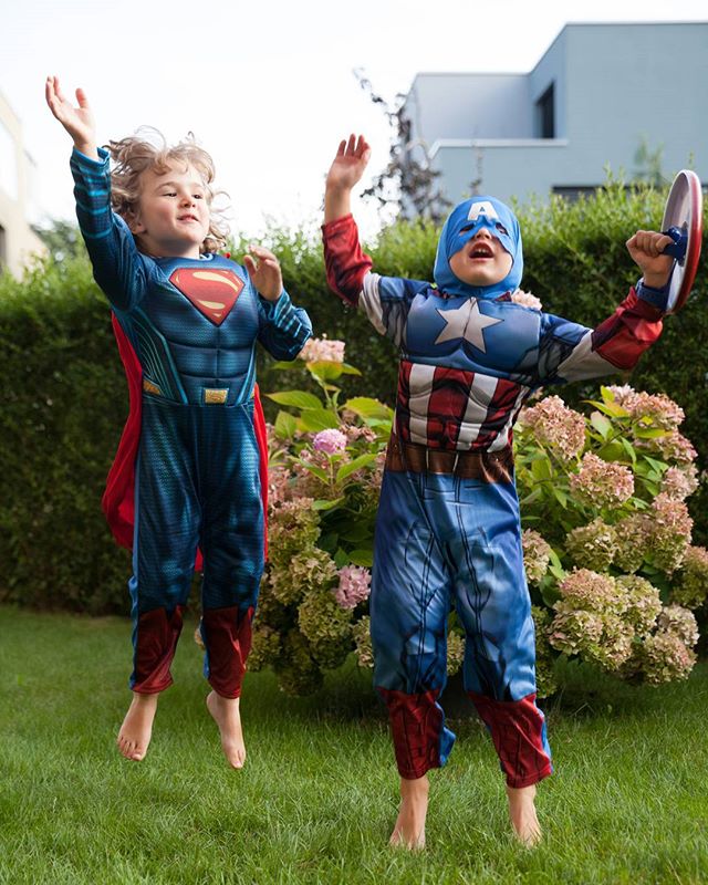 Two young boys dressed in Superman and Captain America costumes play in the yard.
