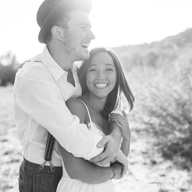 A happy couple embraces in a sunlit field, their smiles radiating love and joy in a timeless black and white photo.