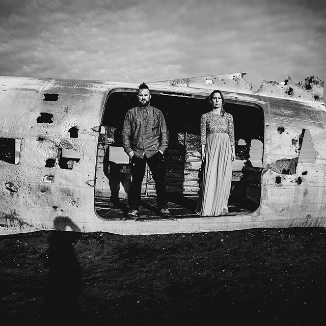 A couple stands in front of an airplane wreck in black and white, a striking image perfect for travel blogs.