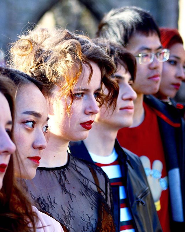 A diverse group of young people stand in a line, looking forward with serious expressions.