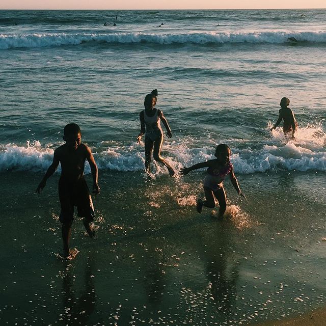 Four children are playing in the waves at the beach during a warm summer sunset.