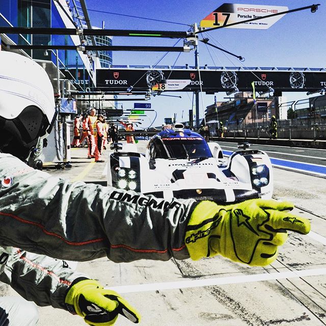 A racing team prepares for a pit stop during a motorsport event with a Porsche race car.