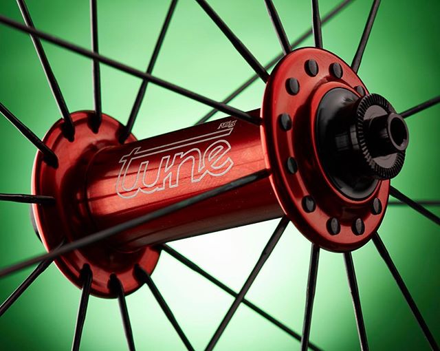 Close-up of a red Tune bicycle hub with black spokes against a soft green background.